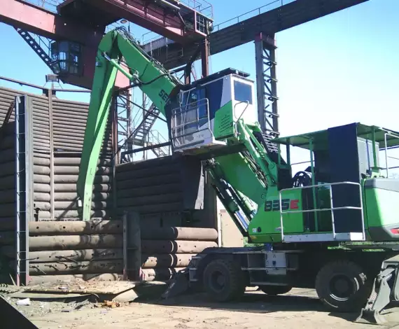 Eine grüne Maschine ist im Einsatz, um einen Stapel Metallschrott zu bearbeiten.