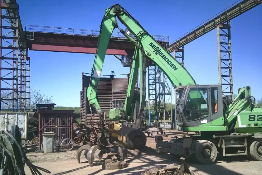Eine grüne Maschine bearbeitet einen Metallhaufen auf einer Baustelle.