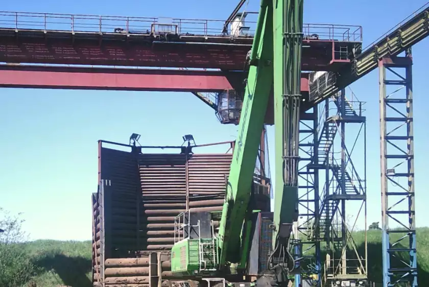 Eine grüne Maschine ist im Einsatz, um einen Stapel Metallschrott zu bearbeiten.