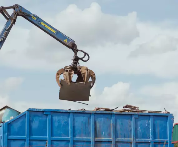 Ein Kran transportiert einen großen blauen Container, der für die Entsorgung genutzt wird.