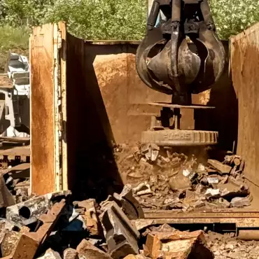 Eine große Maschine bearbeitet einen Haufen Schrottmetall auf einer Baustelle.