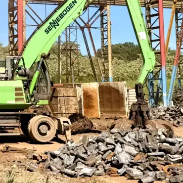 Ein grüner Bagger arbeitet an einem Metallhaufen auf einer Baustelle.