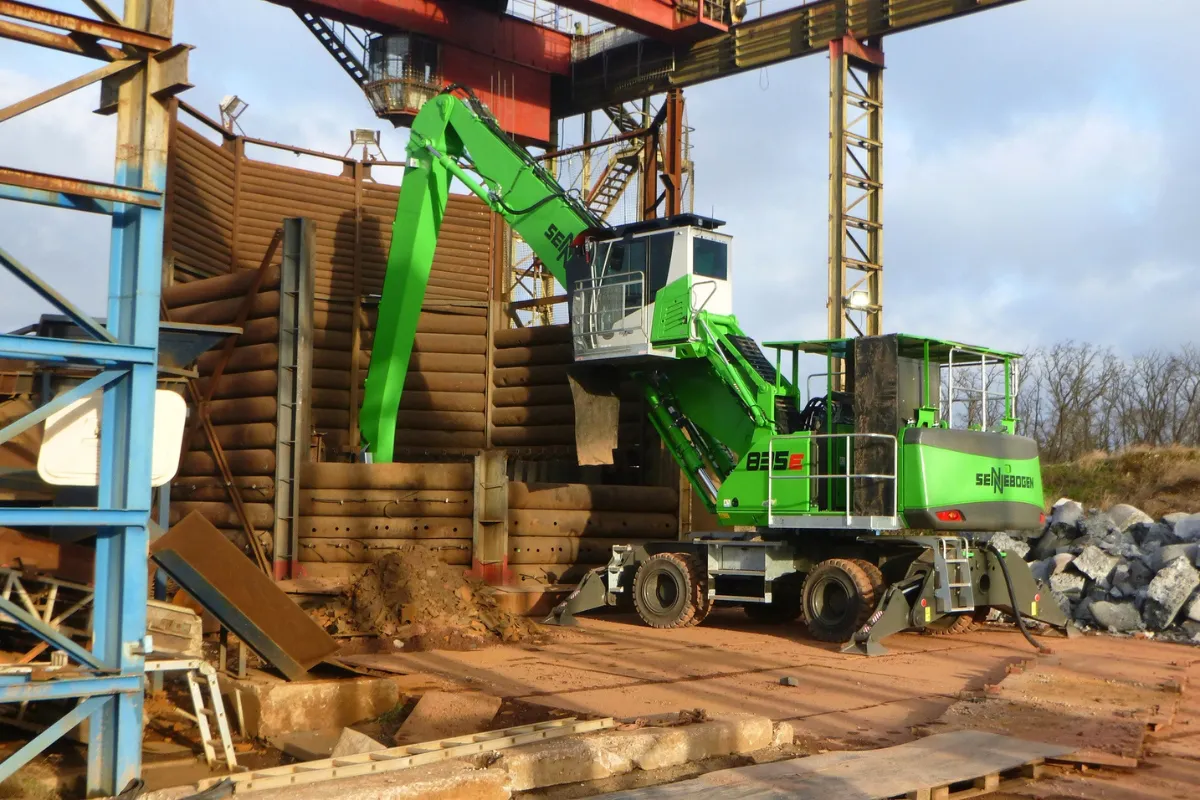Ein umweltfreundlicher Materialumschlagbagger ist auf einer Baustelle im Einsatz und hebt mit seinem ausgefahrenen Arm Materialien in der Nähe von Holzkonstruktionen an.