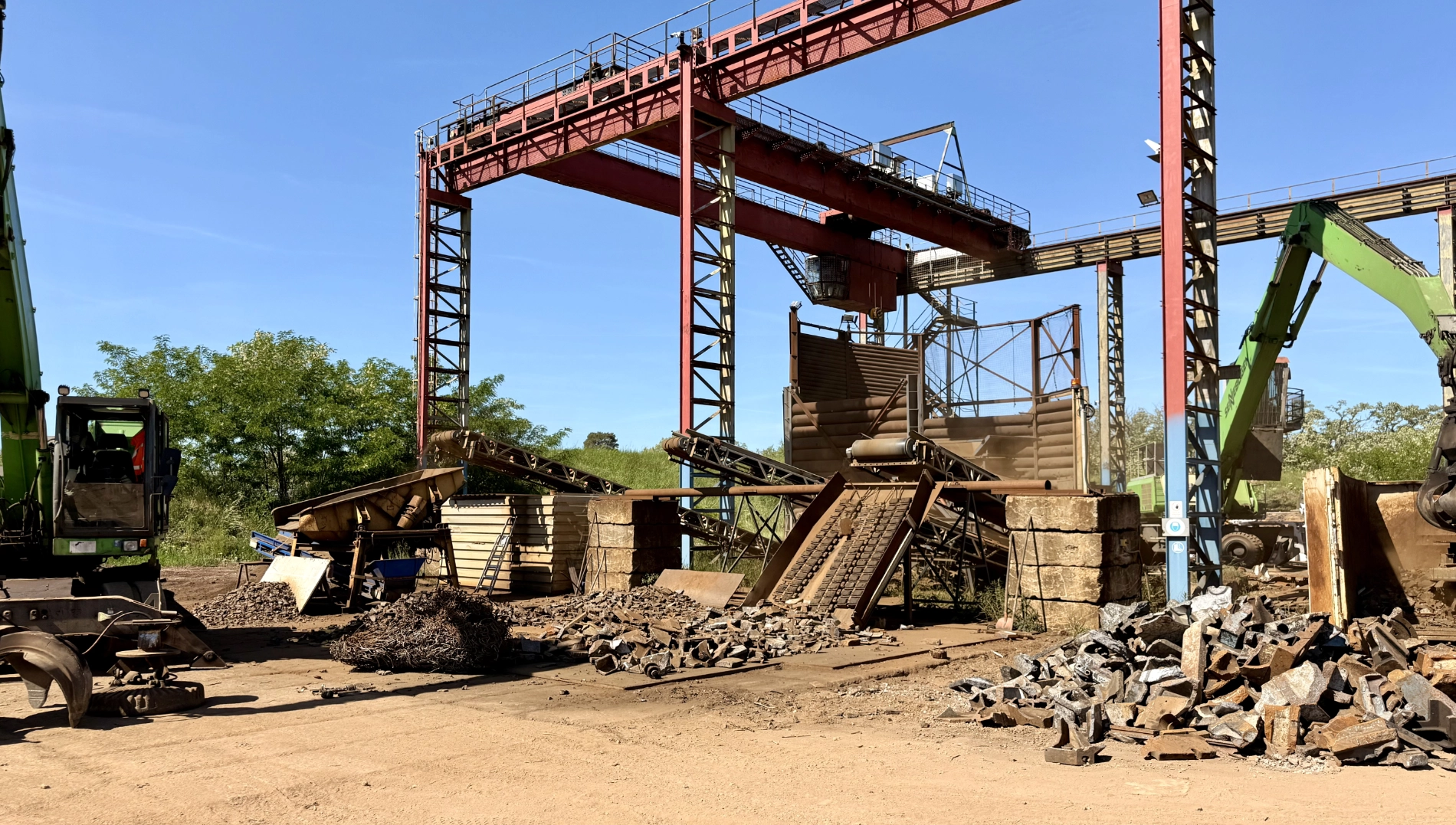 Schwere Maschinen und große Metallkonstruktionen auf einer Baustelle unter klarem blauem Himmel.