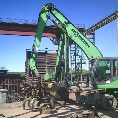 Eine grüne Maschine bearbeitet einen Metallhaufen auf einer Baustelle.