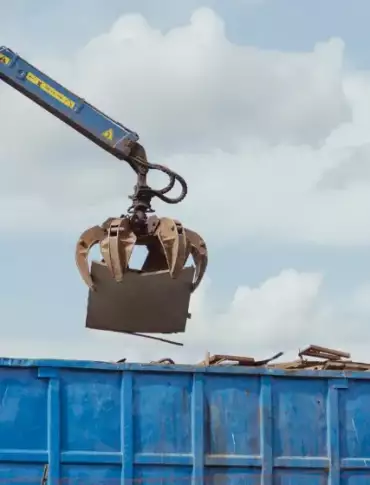 Ein Kran transportiert einen großen blauen Container, der für die Entsorgung genutzt wird.