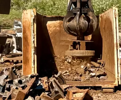 Eine große Maschine bearbeitet einen Haufen Schrottmetall auf einer Baustelle.