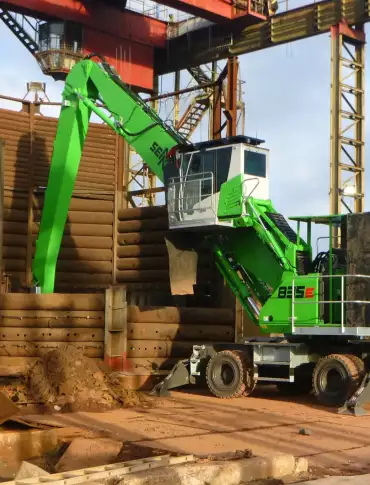Ein umweltfreundlicher Materialumschlagbagger ist auf einer Baustelle im Einsatz und hebt mit seinem ausgefahrenen Arm Materialien in der Nähe von Holzkonstruktionen an.